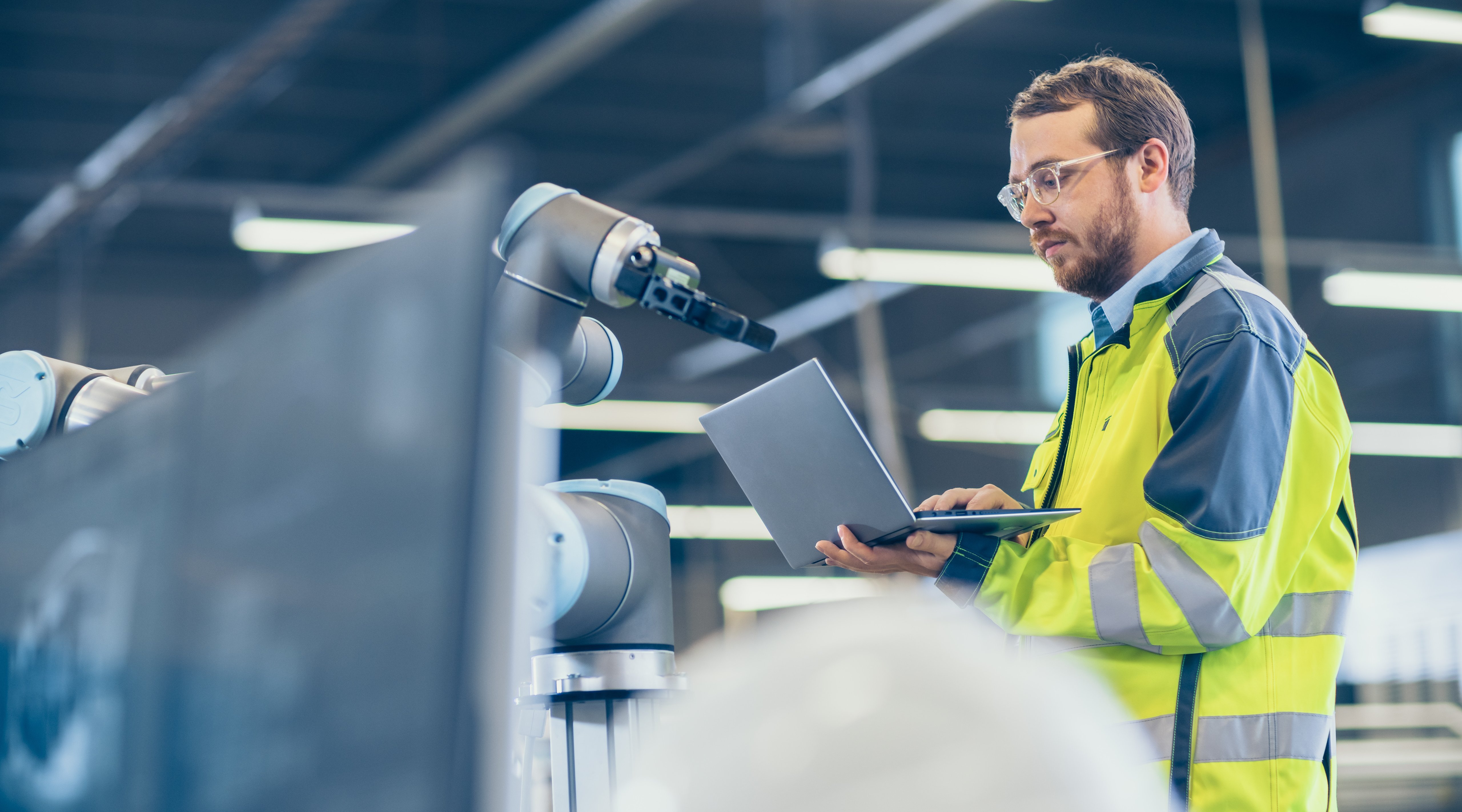 Ingenieur mit Laptop prüft Roboterarm in automatisierter Fertigungshalle